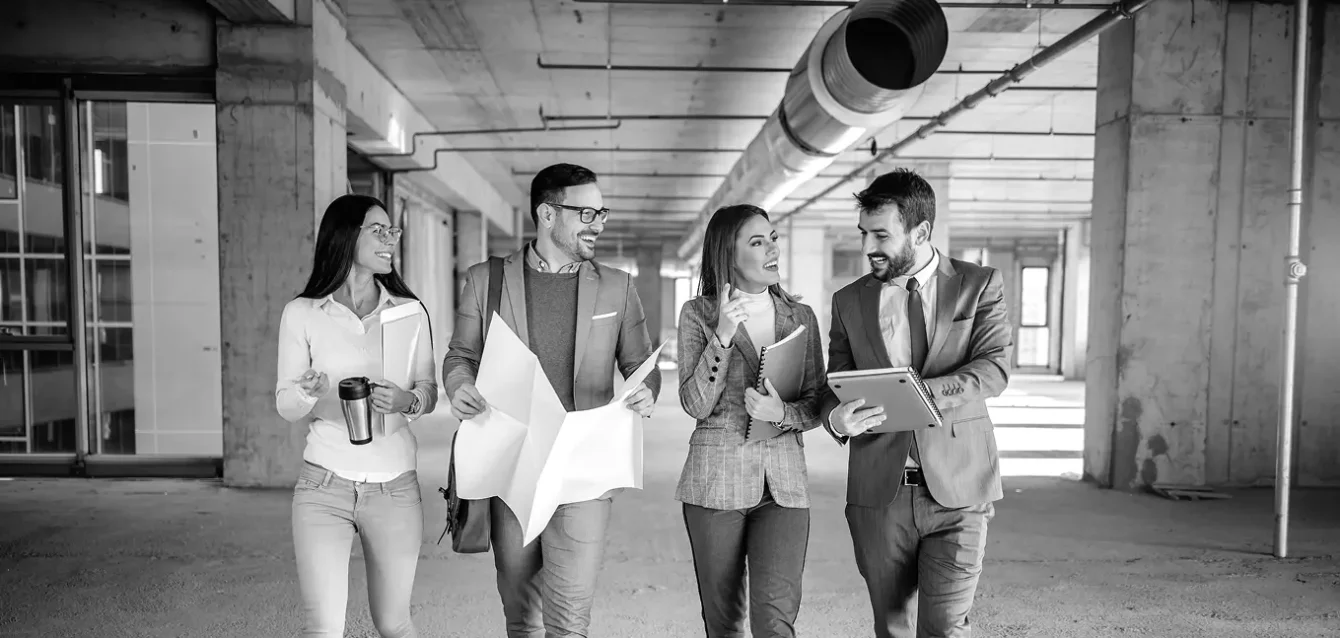 Four professionals walking through a commercial space, reviewing plans and data—representing collaborative CRO audit strategy and client delivery.